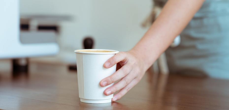 A barista slides a white paper coffee cup toward the outer edge of a coffeeshop counter.